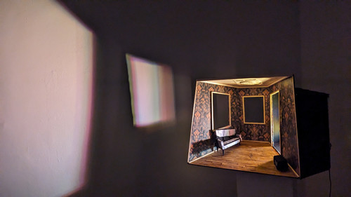 model of minature sitting room lit from within casting a shadow on the wall