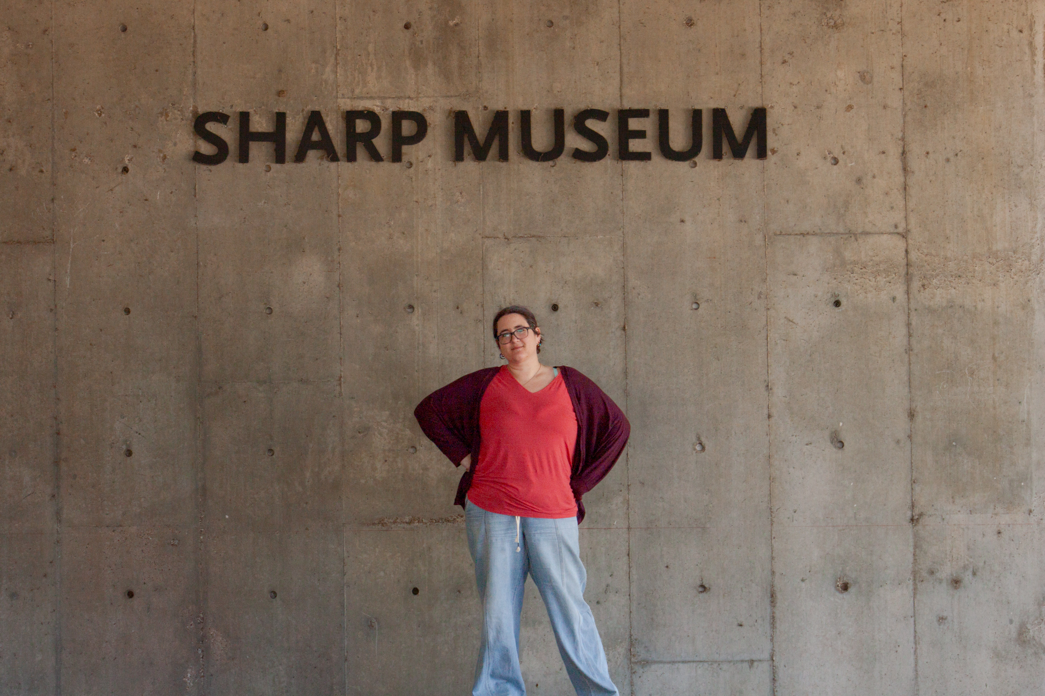 T Lance in an orange shirt and blue jeans standing infront of the sharp museum sign